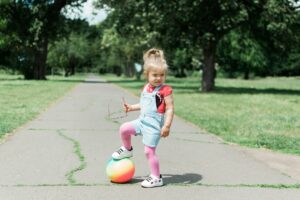 Kind spielt draußen mit einem Ball auf einem Weg